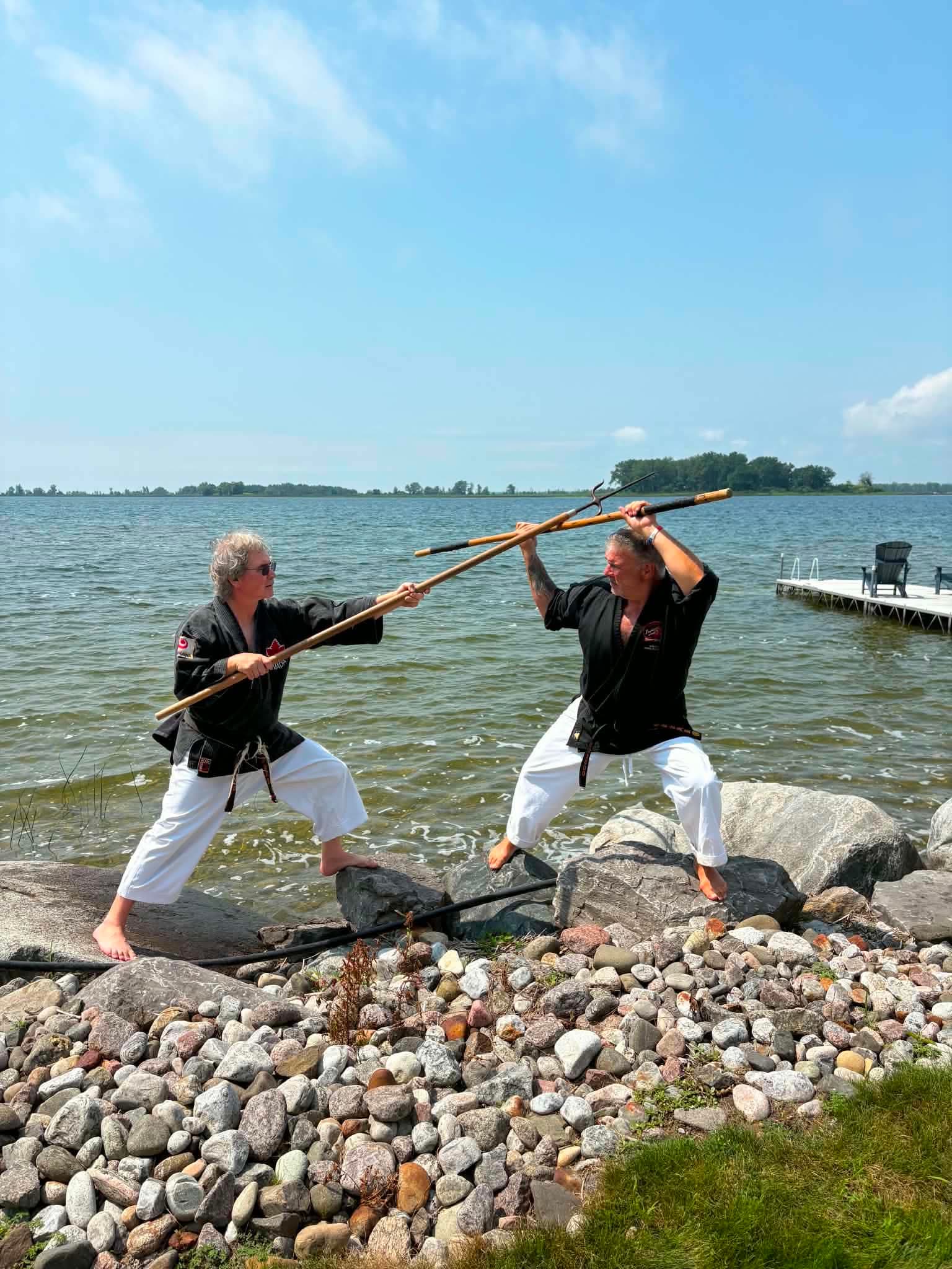 Deux pratiquants en duel de bâtons sur le bord de l'eau